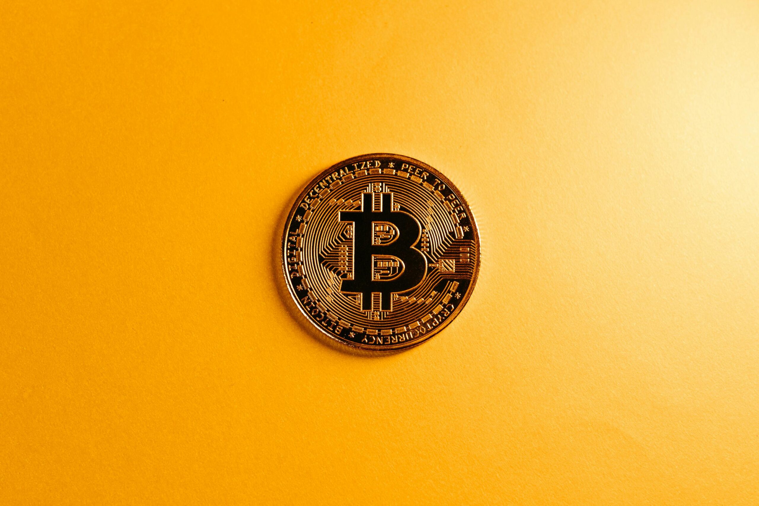 A close-up of a Bitcoin coin on a bright yellow background, symbolizing digital currency.